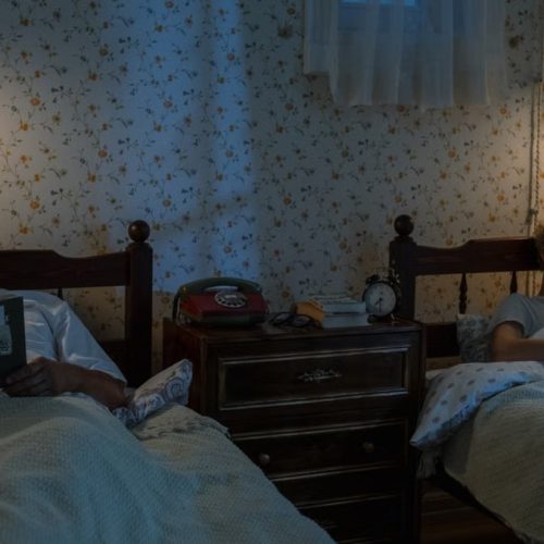 A senior man and young boy enjoy reading in bed at night in a cozy bedroom.