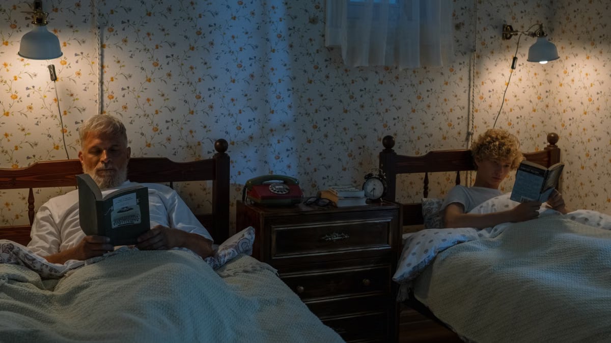 A senior man and young boy enjoy reading in bed at night in a cozy bedroom.